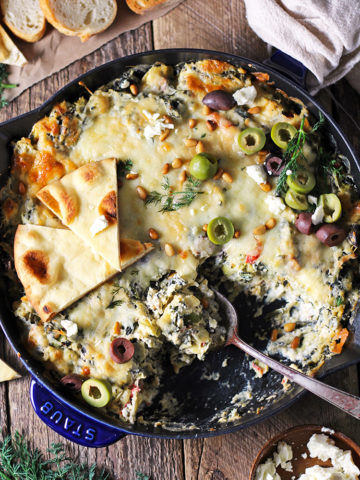 Mediterranean Spinach Artichoke Dip is baked to creamy, cheesy perfection and served with toasted pita bread. Bursting with flavor from spinach, artichokes, olives, and feta cheese, this easy dip is a party favorite!