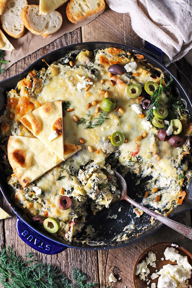 Mediterranean Spinach Artichoke Dip is baked to creamy, cheesy perfection and served with toasted pita bread. Bursting with flavor from spinach, artichokes, olives, and feta cheese, this easy dip is a party favorite!