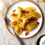 Easy, homemade, tender pasta dough filled with crispy bacon, sharp cheddar cheese and creamy, buttery mashed potatoes. The best comfort food!! Boil the pierogies then sauté in butter and olive oil till golden, delicious perfection. Season with salt and pepper, drizzle with more butter, and top with crumbled bacon and chives.