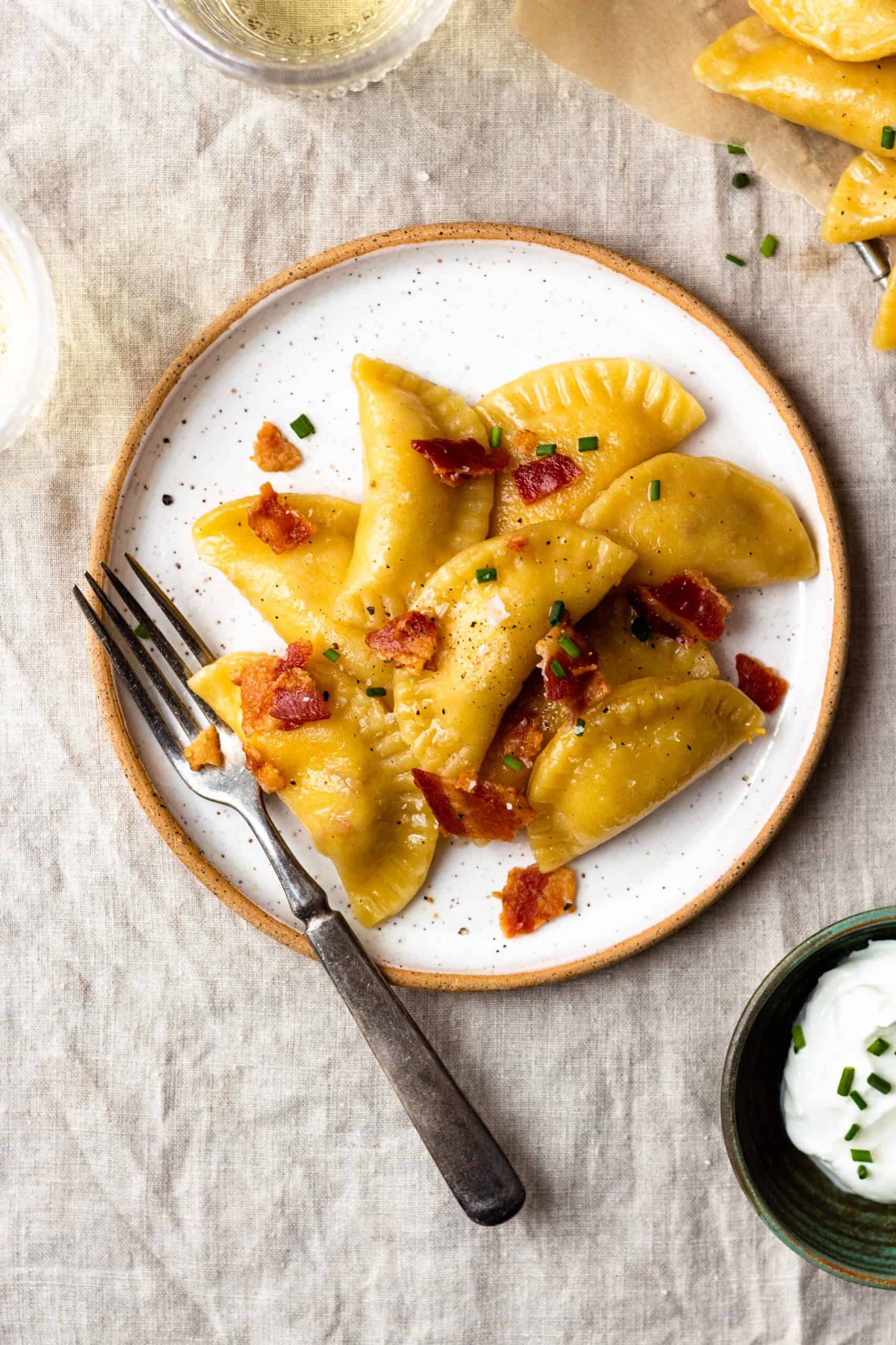 Easy, homemade, tender pasta dough filled with crispy bacon, sharp cheddar cheese and creamy, buttery mashed potatoes. The best comfort food!! Boil the pierogies then sauté in butter and olive oil till golden, delicious perfection. Season with salt and pepper, drizzle with more butter, and top with crumbled bacon and chives.