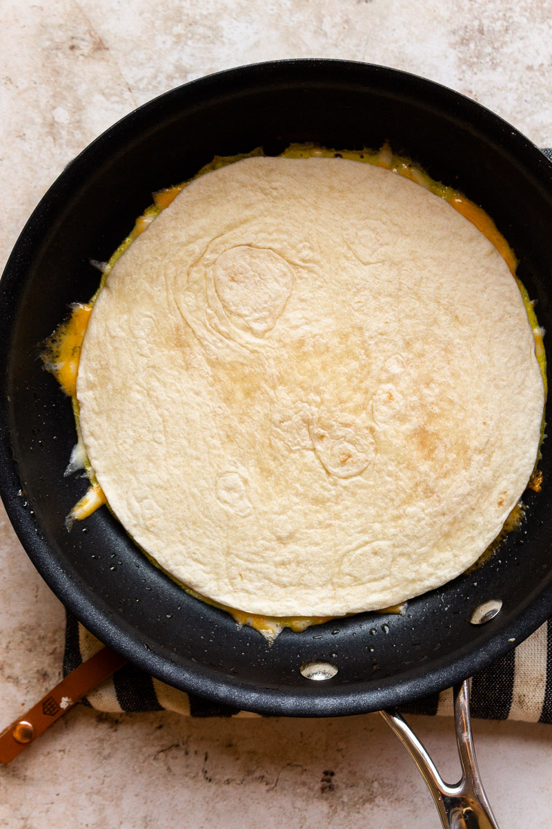 tortilla over egg and cheese in a pan