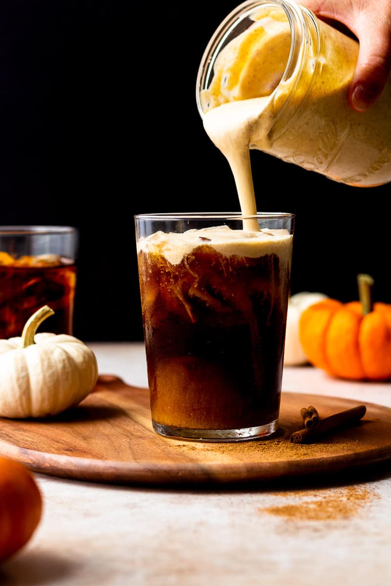 pouring pumpkin foam over iced cold brew coffee