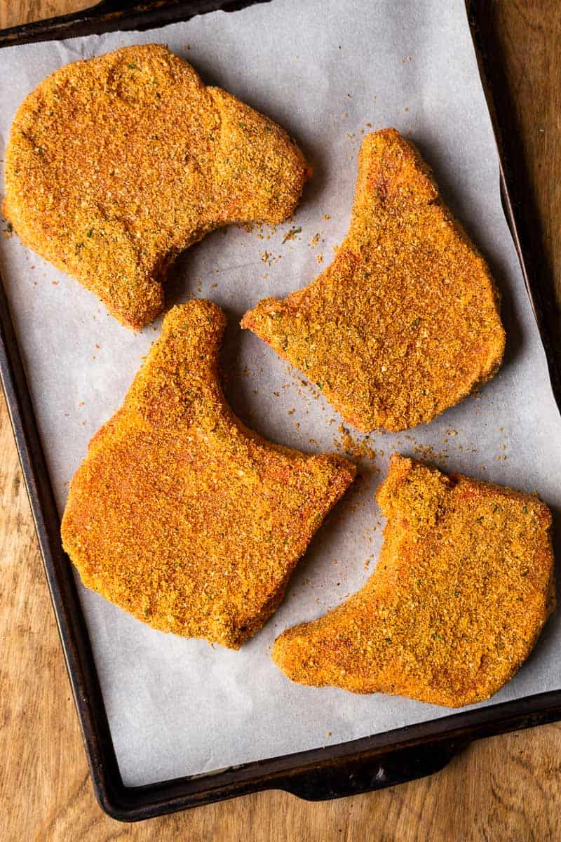 pork chops coated in breading on sheet pan