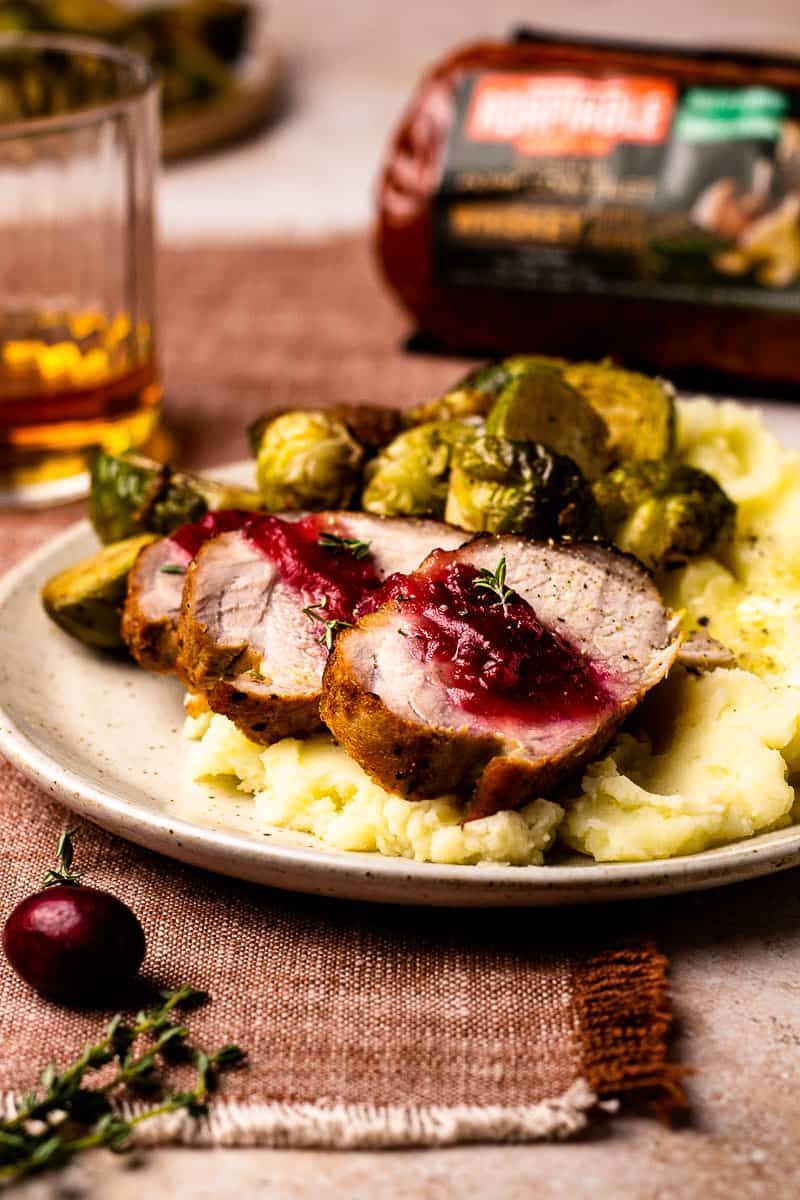 sliced pork tenderloin on a plate with brussel sprouts and mashed potatoes