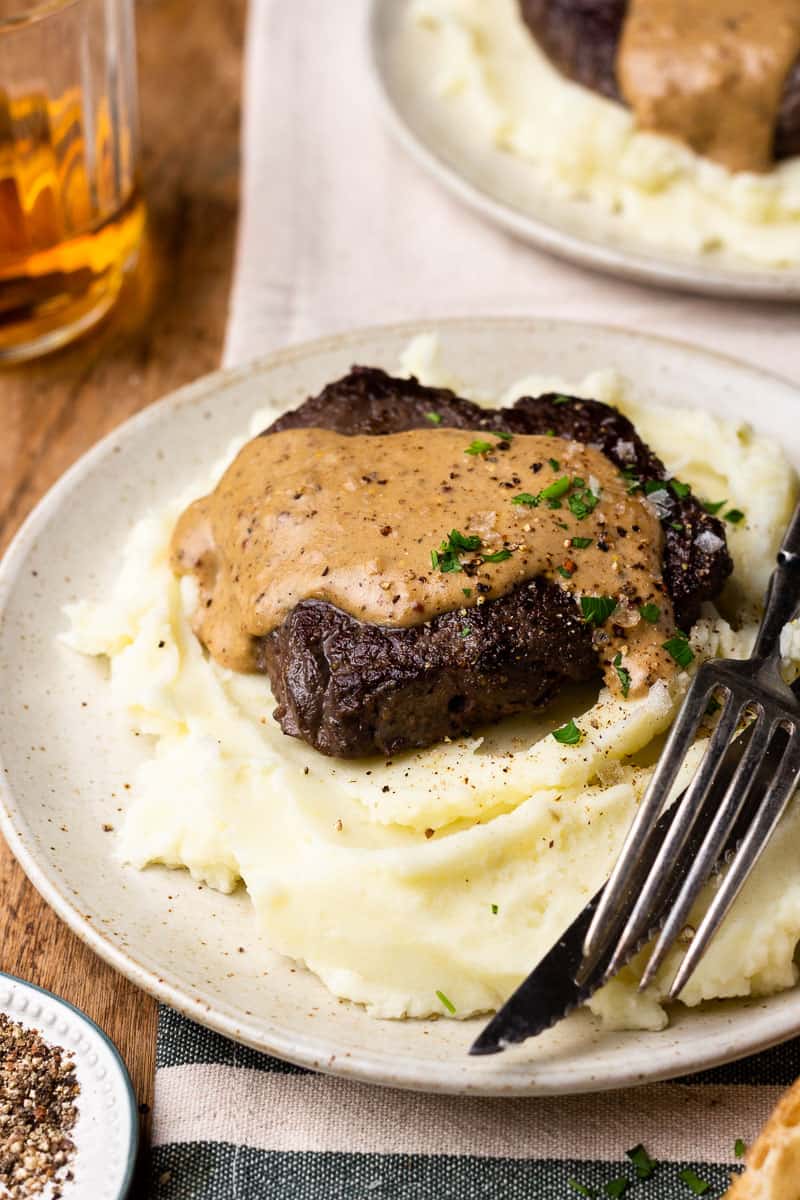 sirloin steak on a plate with mashed potatoes and peppercorn cream sauce