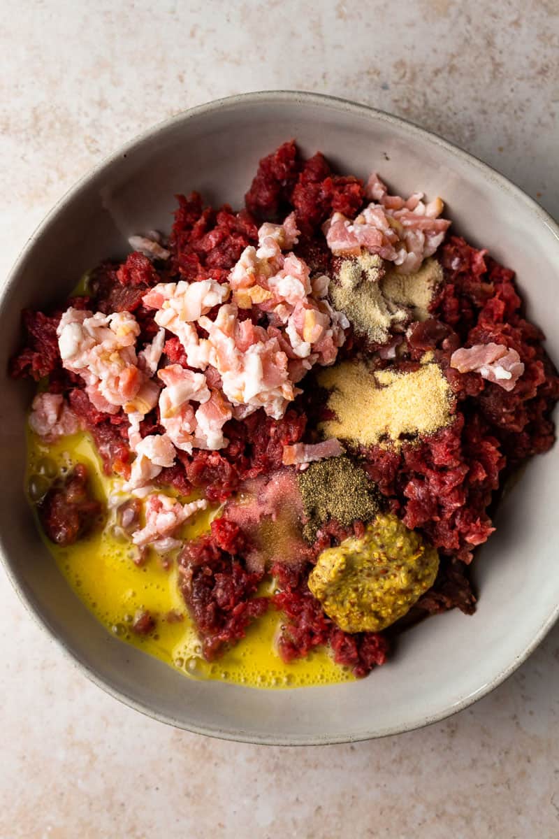 ground venison in a bowl with bacon, egg and seasoning