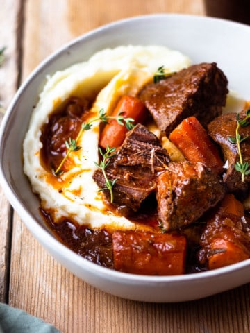 venison roast in a bowl with carrots and mashed potatoes