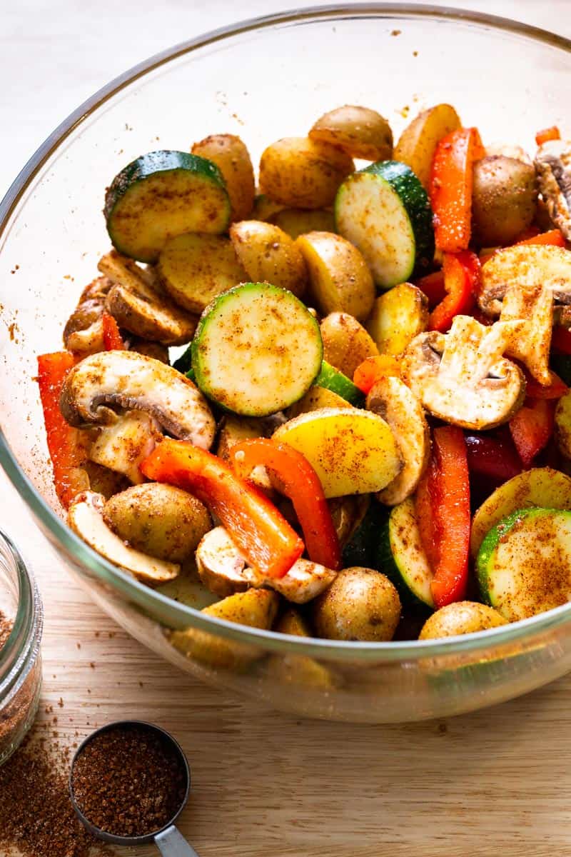 potatoes, peppers, mushrooms and zucchini in a bowl with BBQ seasoning