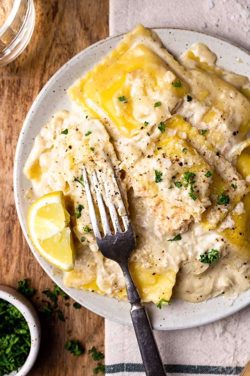 lobster ravioli with lemon cream sauce on a plate with one ravioli cut in half and served with white wine