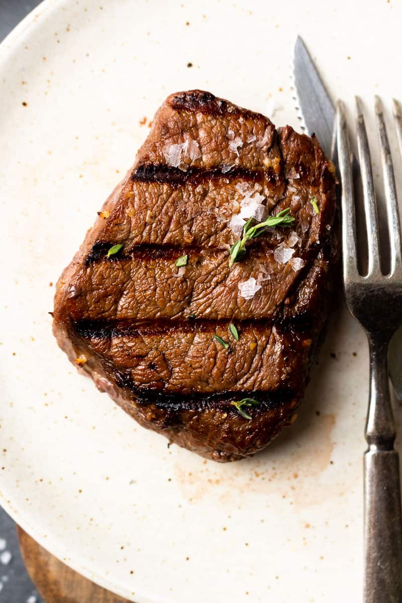 grilled marinated elk steak on a plate with a fork and knife