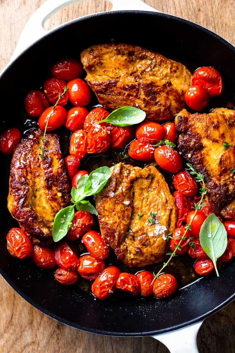 Seared chicken and tomatoes in a skillet with fresh thyme and basil
