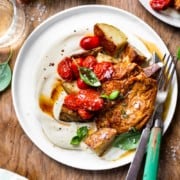 Chicken, potatoes, burst cherry tomatoes and whipped feta on a plate with a glass of white wine