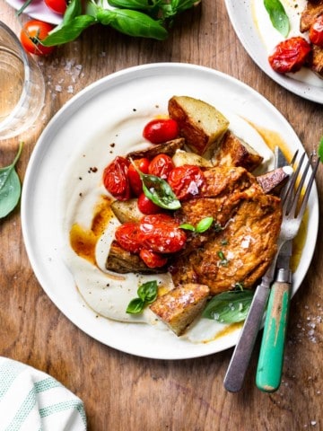 Chicken, potatoes, burst cherry tomatoes and whipped feta on a plate with a glass of white wine