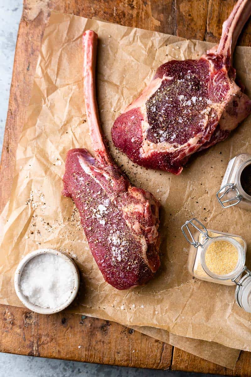 bison tomahawk steaks on a cutting board and seasoned with salt, pepper and garlic powder
