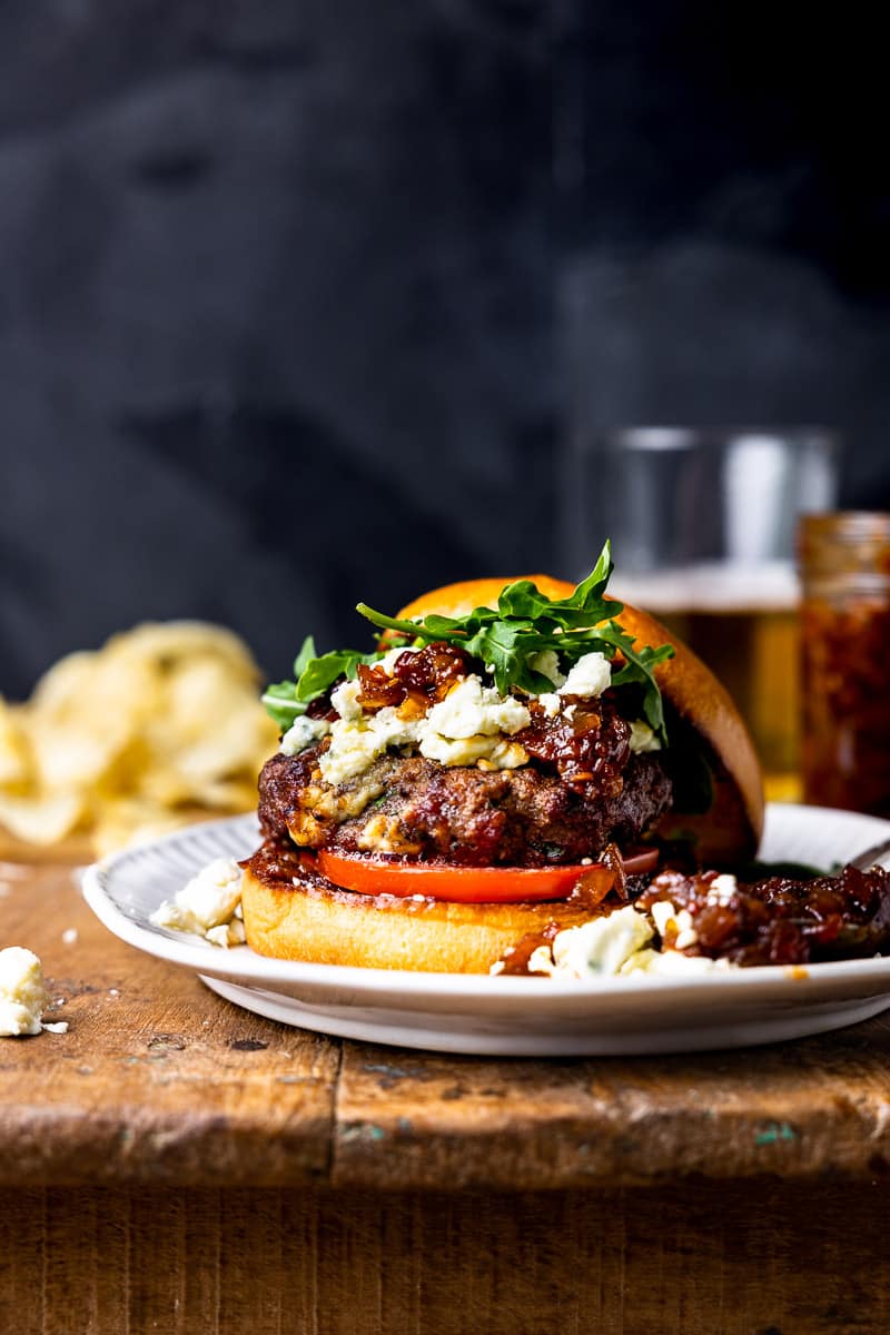 burger on a plate next to a glass of beer and a jar of tomato bacon jam