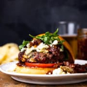 burger on a plate next to a glass of beer and a jar of tomato bacon jam