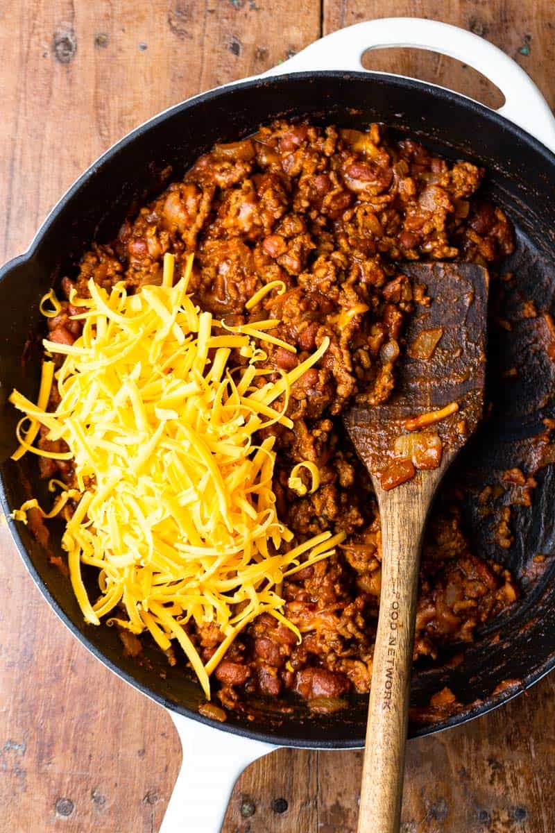 chili cheese sloppy joe meat in a skillet topped with shredded cheddar cheese