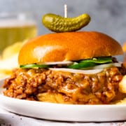 chili cheese sloppy joe meat between a hamburger bun served on a plate with potato chips