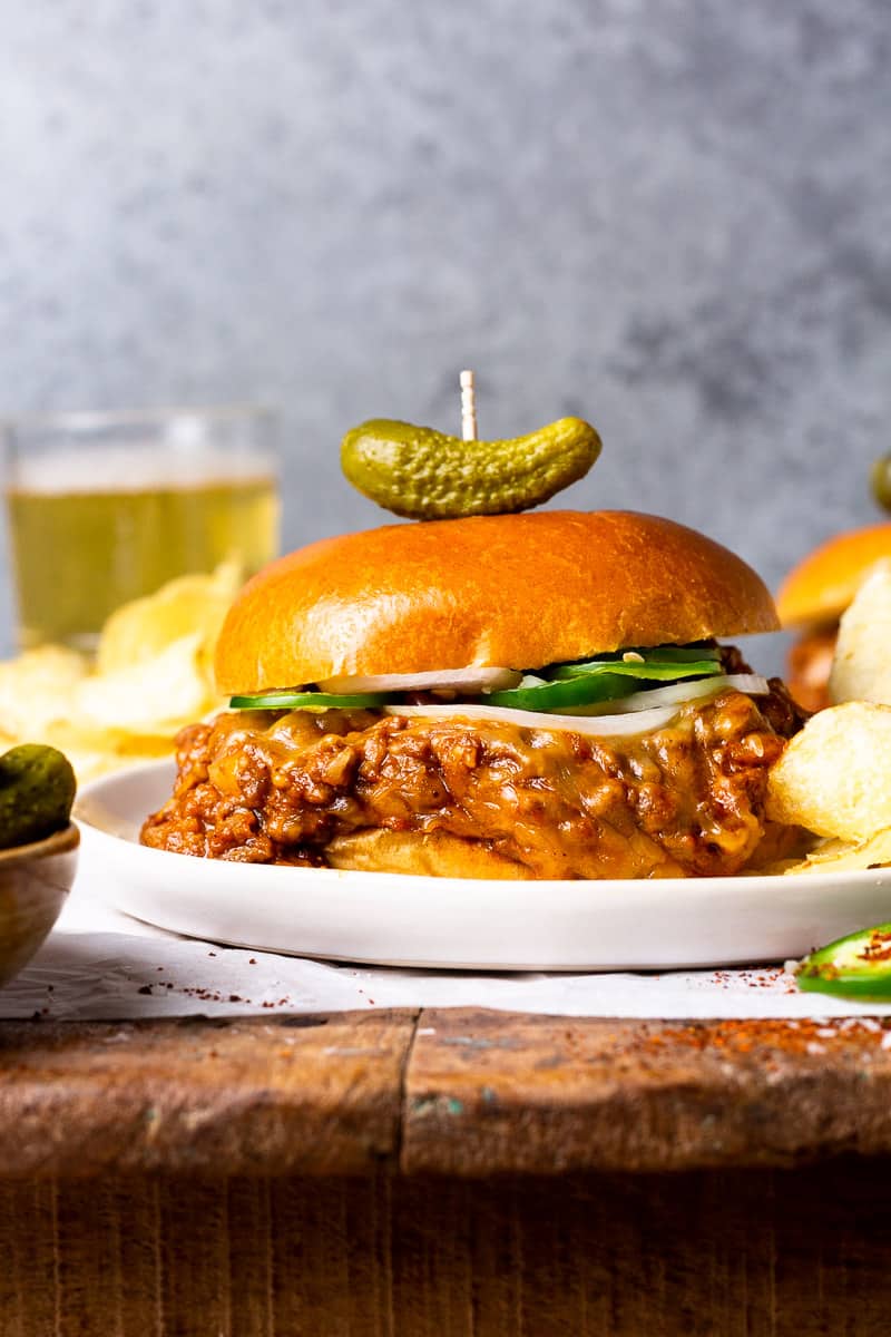 chili cheese sloppy joe meat between a hamburger bun served on a plate with potato chips