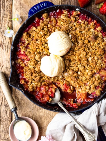Strawberry rhubarb crisp in a skillet and topped with vanilla ice cream
