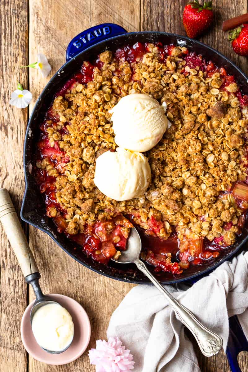 Strawberry rhubarb crisp in a skillet and topped with vanilla ice cream