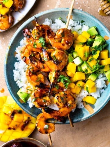 chipotle honey butter shrimp skewers served over a bowl of rice with mango avocado salsa
