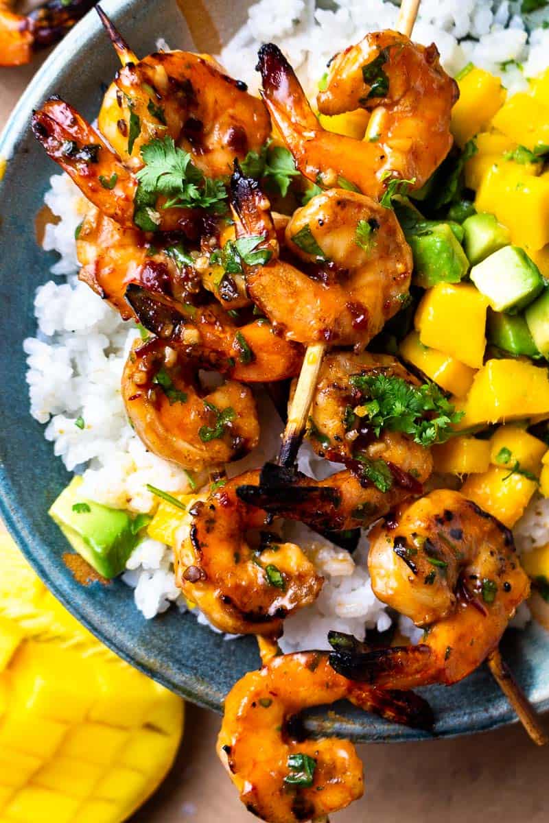 chipotle honey butter shrimp skewers served over a bowl of rice with mango avocado salsa