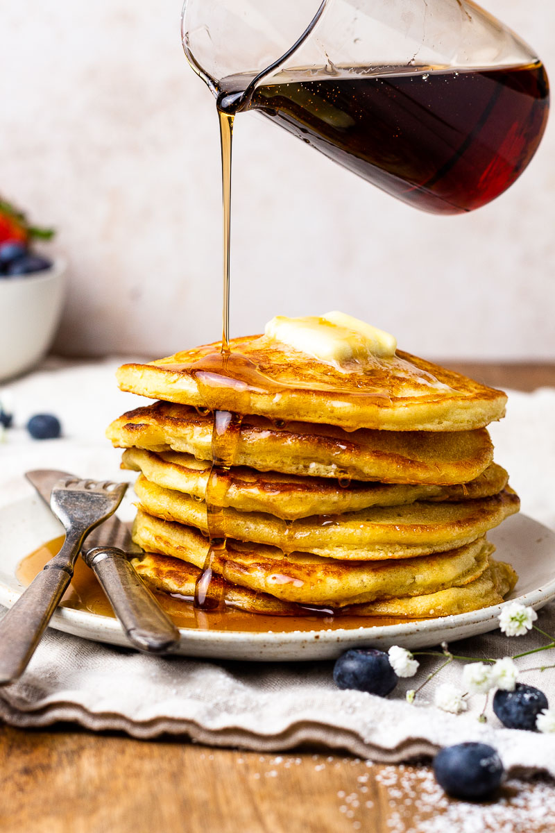 pouring syrup over a stack of sourdough pancakes on a plate