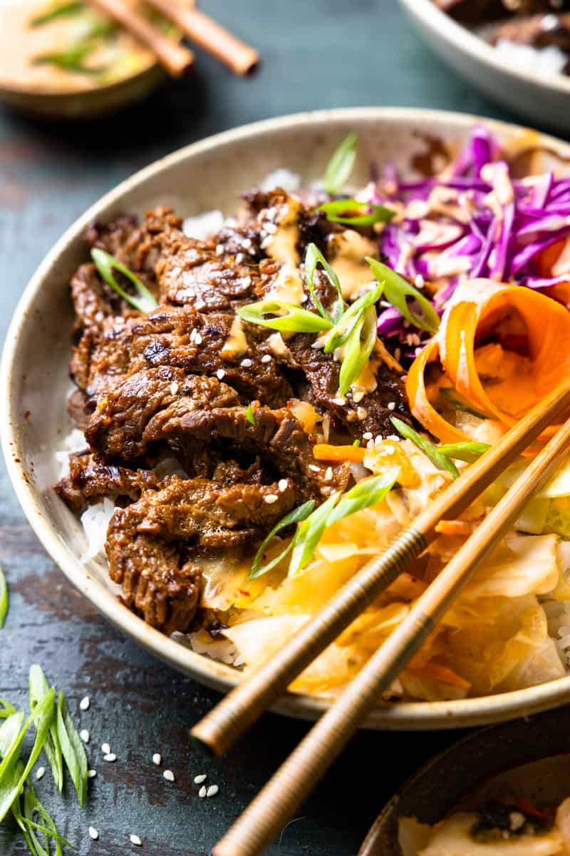 bulgogi skirt steak served in a bowl over a bed of rice with fresh vegetables, kimchi and green onions