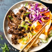 bulgogi skirt steak served in a bowl over a bed of rice with fresh vegetables, kimchi and green onions