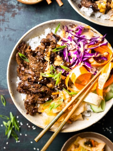 bulgogi skirt steak served in a bowl over a bed of rice with fresh vegetables, kimchi and green onions