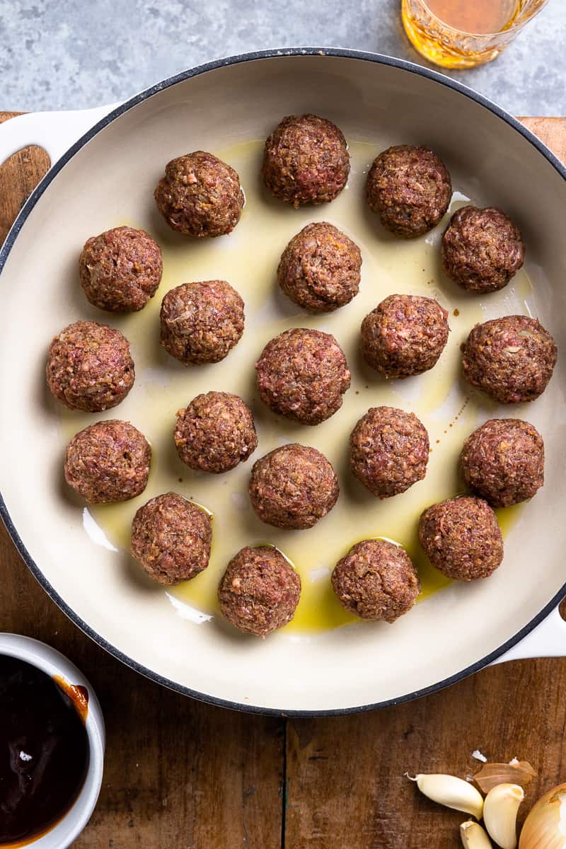 uncooked bison meatballs in a skillet with olive oil
