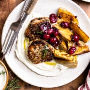 pork tenderloin medallions and roasted potatoes served over whipped goat cheese spread on a plate and topped with cranberry sauce