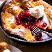 dutch baby in a skillet topped with powdered sugar, spiced cranberries, and whipped cream