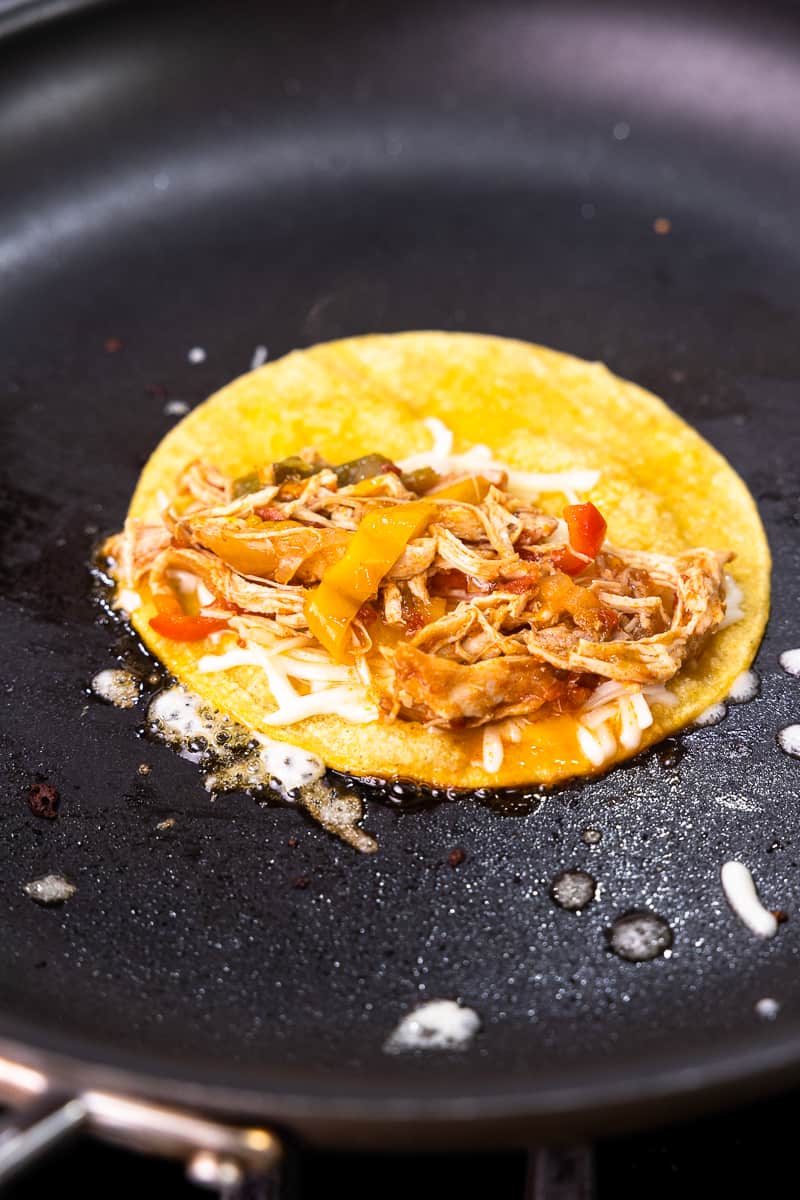 open tortilla in a skillet topped with cheese, chicken and fajita vegetables