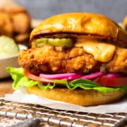 Crispy fried chicken on a bun with aioli and burger toppings. Fried chicken and pickles in the background.
