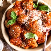 Venison meatballs in a bowl with tomato sauce, parmesan and fresh basil.