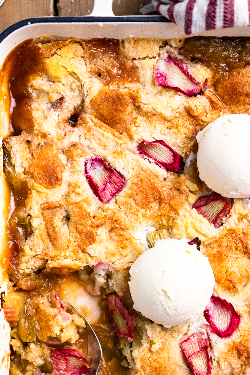 cooked rhubarb dump cake in a baking dish topped with vanilla ice cream