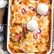 Rhubarb dump cake in a baking dish topped with vanilla ice cream and using a spoon to scoop out cake