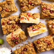 Sliced rhubarb bars on parchment paper next to a large knife and flowers.