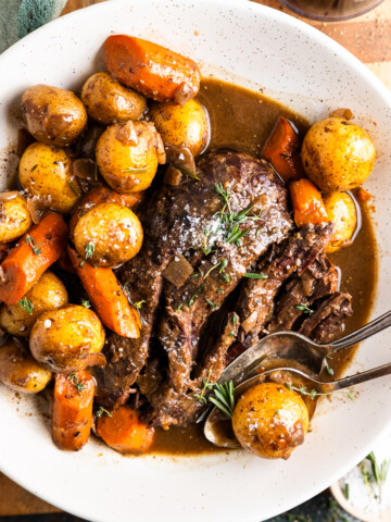 venison roast pulled apart in a serving dish with carrots, potatoes and gravy