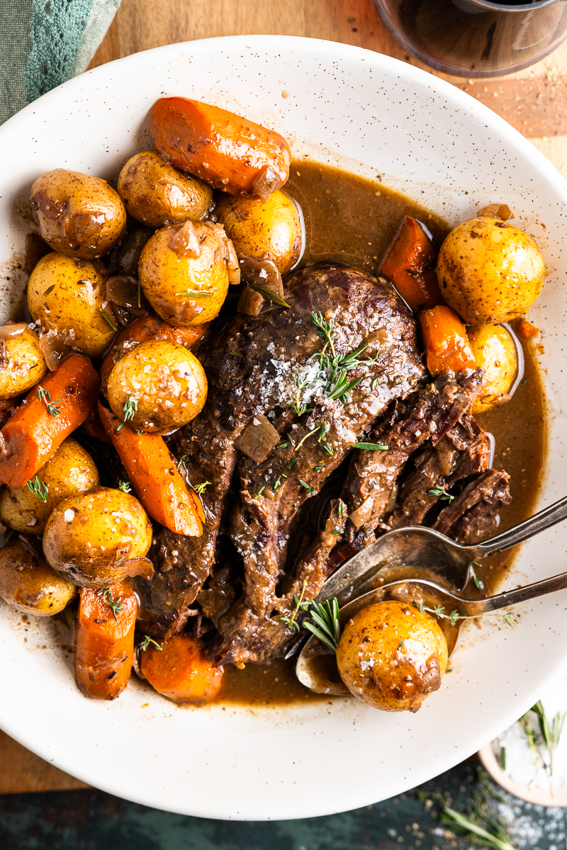 venison roast pulled apart in a serving dish with carrots, potatoes and gravy