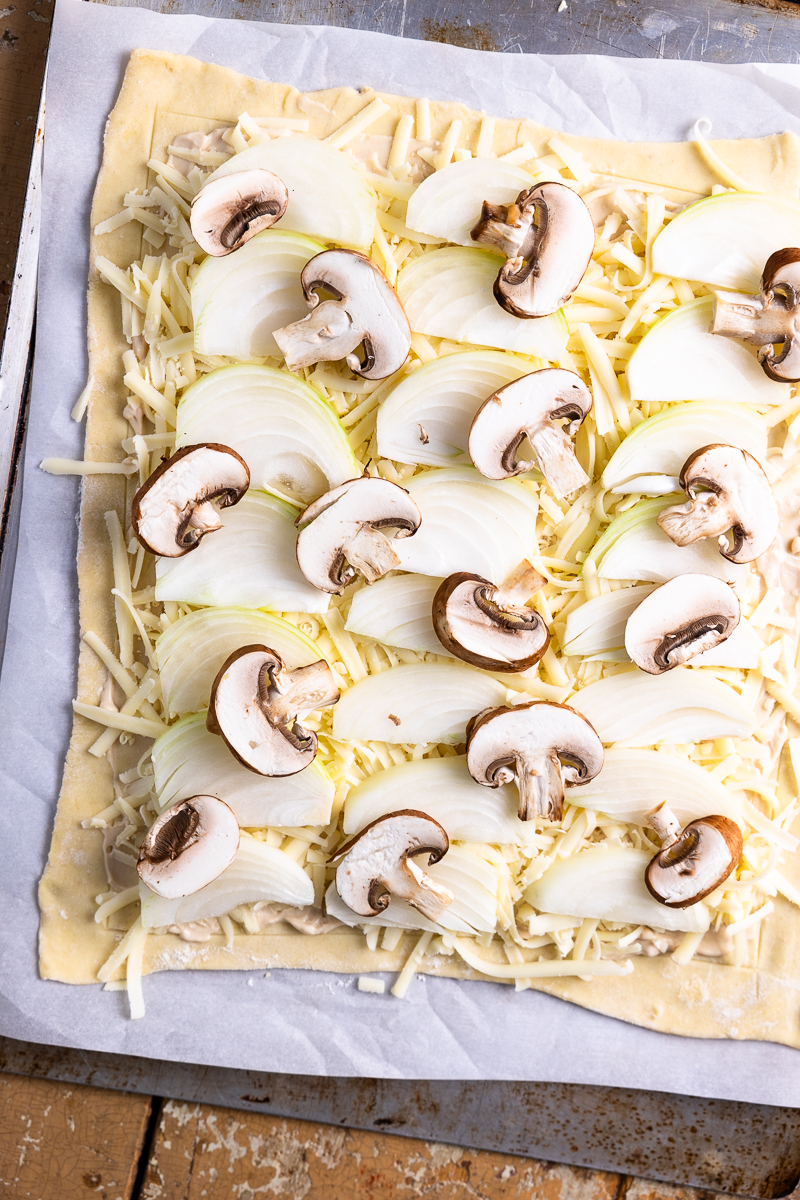 puff pastry spread with French onion dip and topped with white cheddar cheese, onions and mushrooms