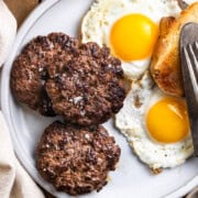 Cooked venison breakfast sausage on a plate with eggs and toast next to a cup of coffee.
