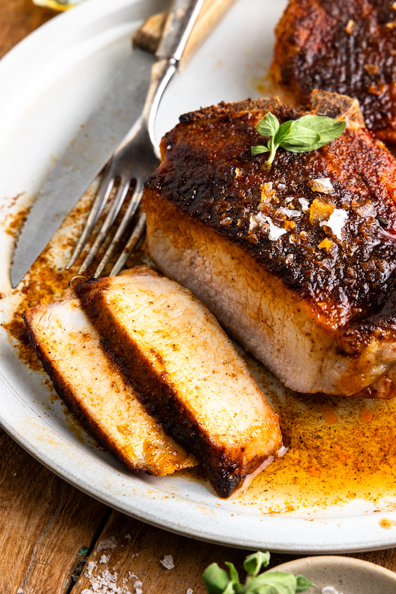 close up of a sliced pork chop on a plate with a knife and fork