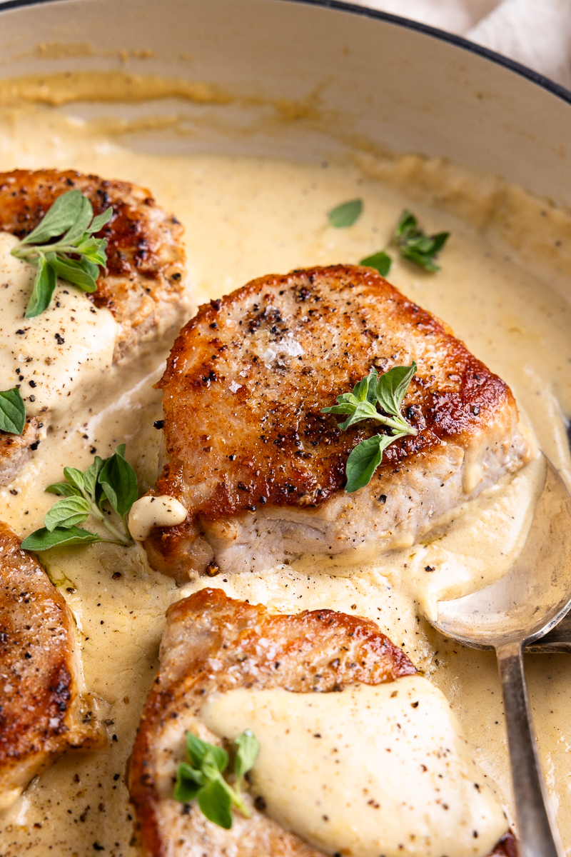 side view of a seared pork chop in a skillet with cream sauce
