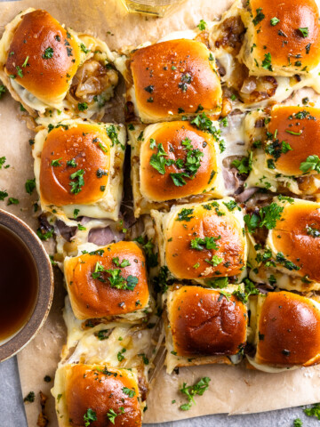 French onion roast beef sliders pulled apart on parchment paper and served with au jus