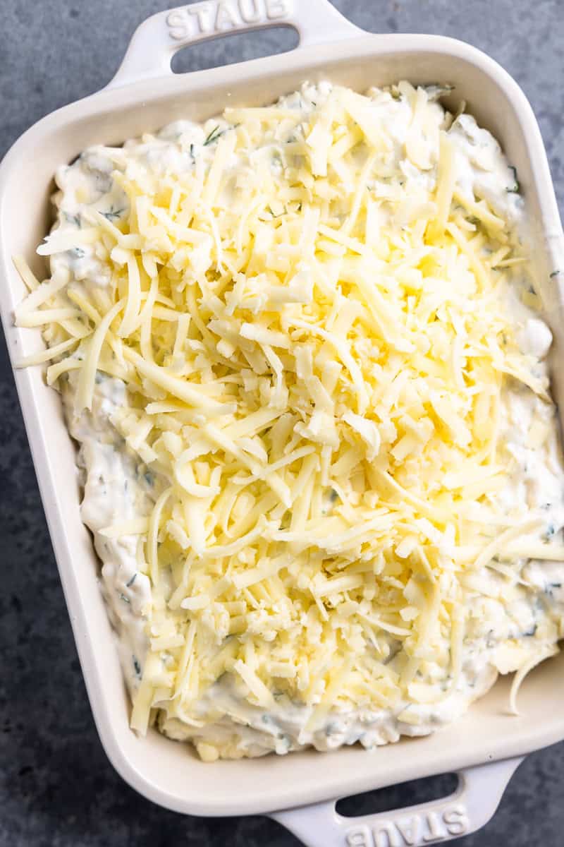 fried pickle dip in a baking dish topped with shredded cheese before it goes into the oven