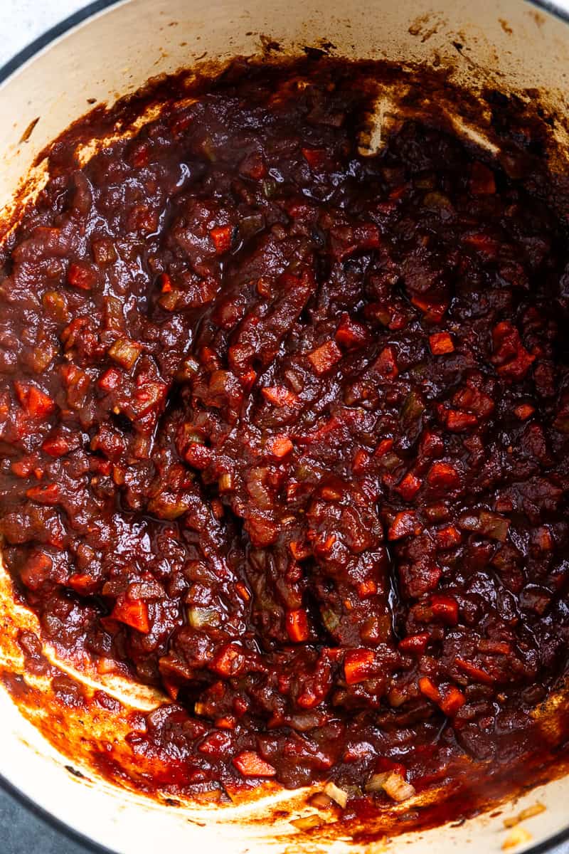 Sautéed vegetables in a pot with tomato paste and red wine