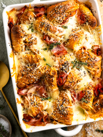 breakfast bake garnished with fresh thyme and sitting on a towel next to a serving spoon and a pinch bowl of salt